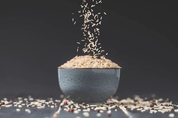 Side view of rice spilling into bowl on black table — Stock Photo