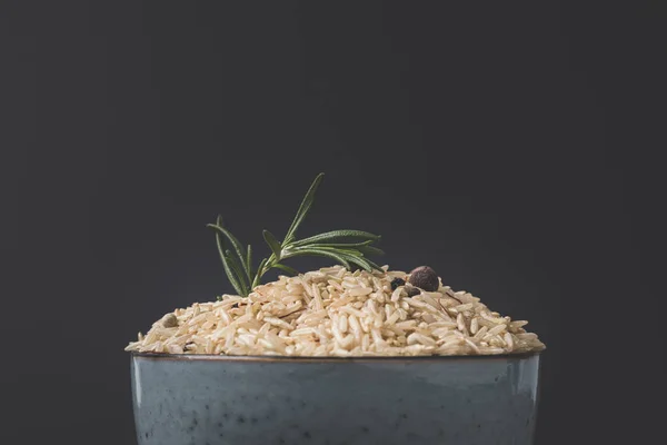 Крупним планом знімок миски сирого рису з розмарином і спеціями на чорній поверхні — стокове фото