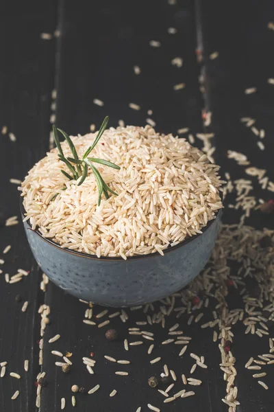 Close-up shot of bowl of raw rice with rosemary on black surface — Stock Photo