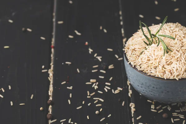 Bowl of raw rice with rosemary on black surface — Stock Photo