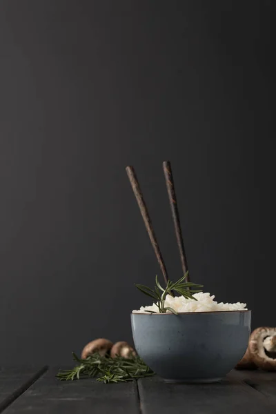 Tigela de arroz saboroso com pauzinhos e cogumelos na mesa preta — Fotografia de Stock