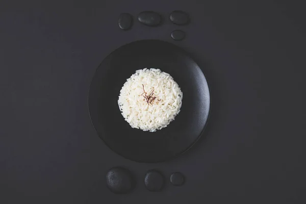 Vue du dessus de riz savoureux sur assiette avec des cailloux sur table noire — Photo de stock