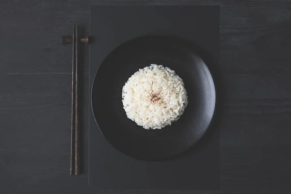 Blick von oben auf leckeren Reis und Stäbchen auf schwarzem Tisch — Stockfoto