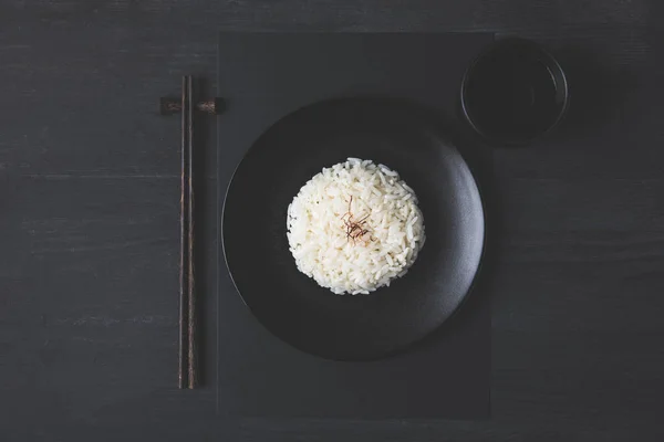 Vista superior de arroz com xícara de chá e pauzinhos na mesa preta — Fotografia de Stock