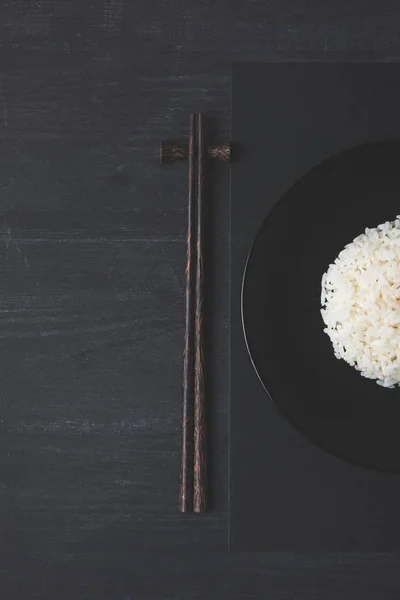Vista superior de arroz y palillos sobre mesa negra - foto de stock