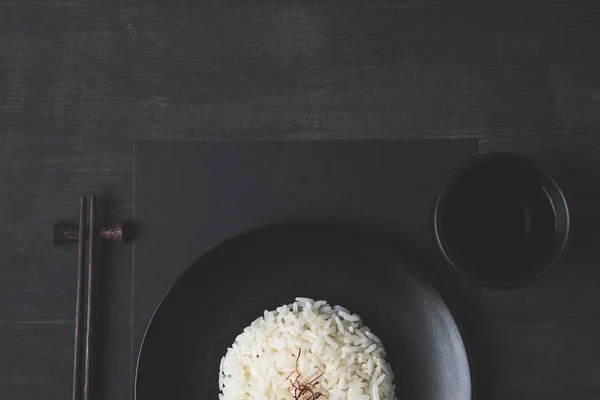 Vista superior del arroz en el plato con taza de té y palillos en la mesa negra - foto de stock