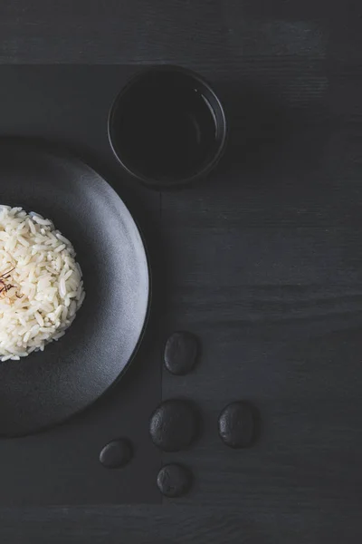 Vista superior del arroz en plato con taza de té sobre mesa negra - foto de stock