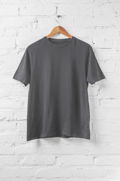 Una camisa gris oscuro en percha en la pared blanca - foto de stock