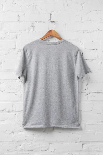 Una camisa gris en percha en la pared blanca - foto de stock