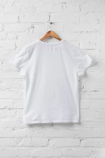 Una camisa blanca en percha en la pared blanca - foto de stock