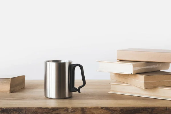 Tasse en argent et livres sur table en bois sur blanc — Photo de stock