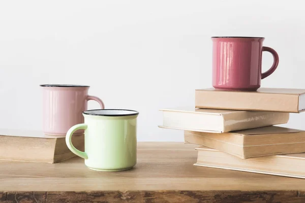 Três copos coloridos e livros sobre mesa de madeira em branco — Fotografia de Stock