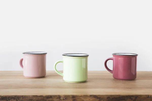 Trois tasses colorées sur table en bois sur blanc — Photo de stock