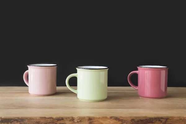 Three colored cups on wooden table on black — Stock Photo