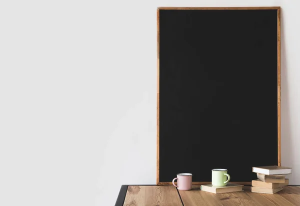 Livros e copos com grande quadro-negro em mesa de madeira em branco — Fotografia de Stock