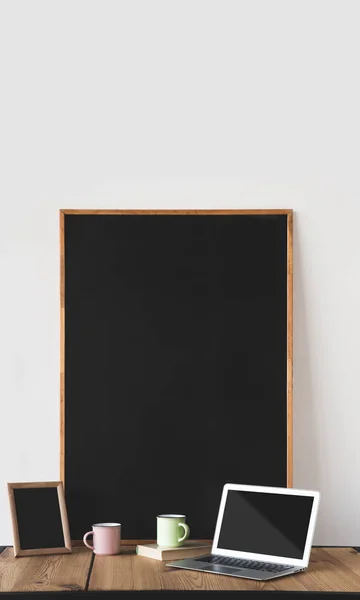 Tableaux noirs vides dans des cadres avec des tasses et un ordinateur portable sur la table sur blanc — Photo de stock