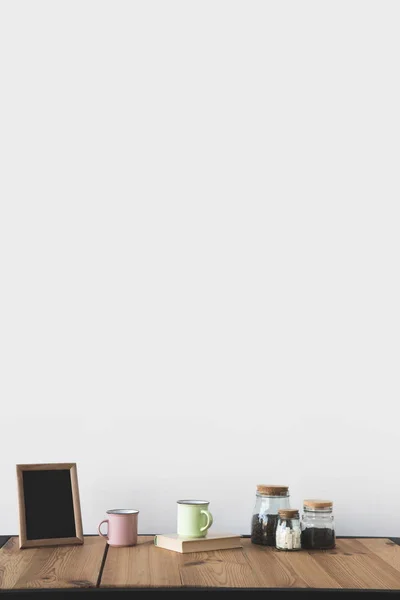 Empty blackboard in frame with cups and coffee on wooden table on white — Stock Photo