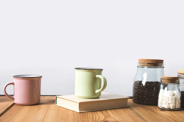 Tasses, livres et bouteilles en verre avec grains de café et sucre raffiné sur la table sur blanc — Photo de stock