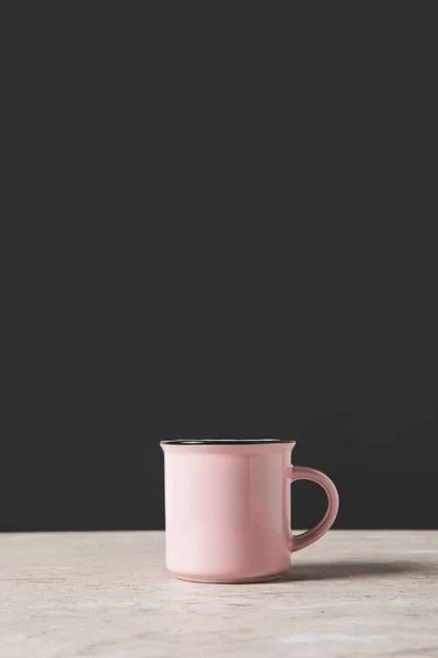 Una taza rosa sobre mesa de mármol sobre negro - foto de stock