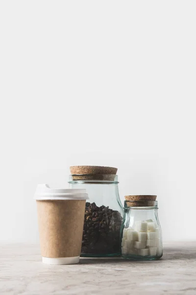 Grains de café, sucre raffiné et tasse à café jetable sur table en marbre blanc — Photo de stock