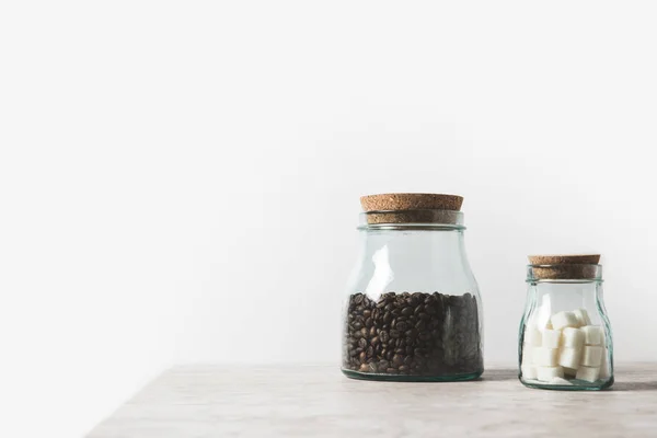 Grains de café et sucre raffiné en bouteilles de verre sur table en marbre blanc — Photo de stock