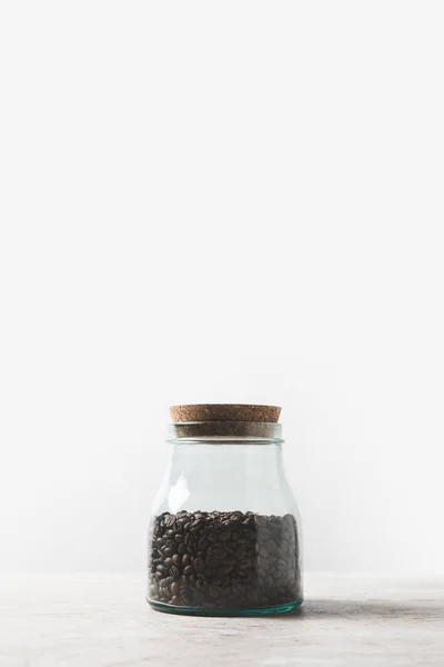 Granos de café en botella de vidrio sobre mesa de mármol sobre blanco - foto de stock