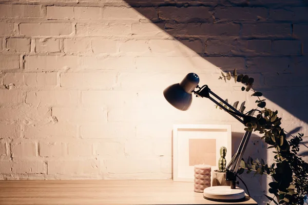 Lâmpada de mesa iluminando parede de tijolo branco vazio, conceito mockup — Fotografia de Stock