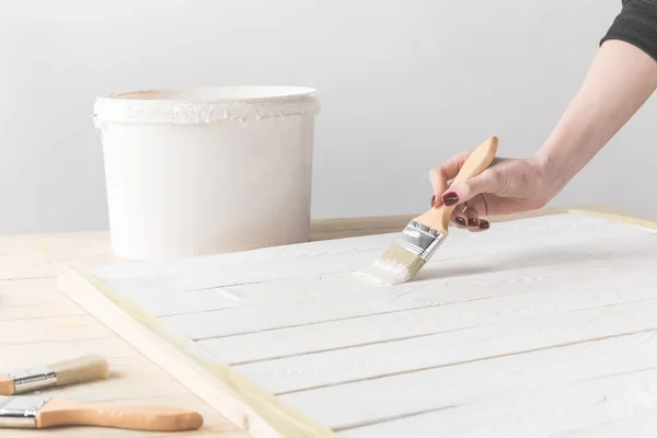 Imagem recortada de mulher pintando mesa de madeira com tinta branca — Fotografia de Stock