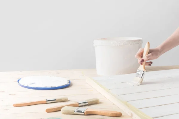 Обрізане зображення дівчини, що малює дерев'яну поверхню з білою фарбою — стокове фото