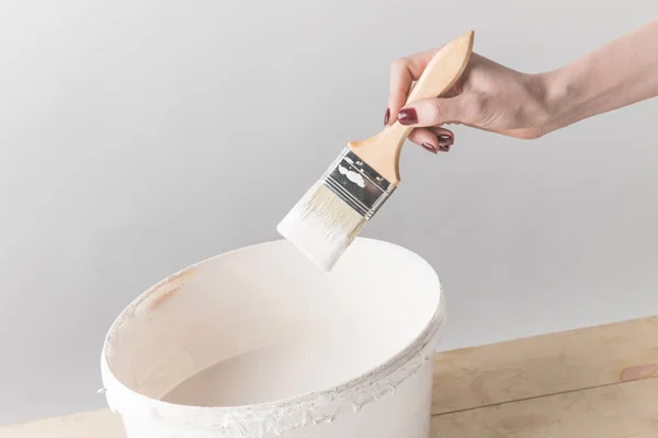 Cropped image of woman holding brush in white paint above bucket — Stock Photo