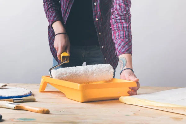 Cropped image of woman putting paint roll brush in white paint at wooden table — Stock Photo