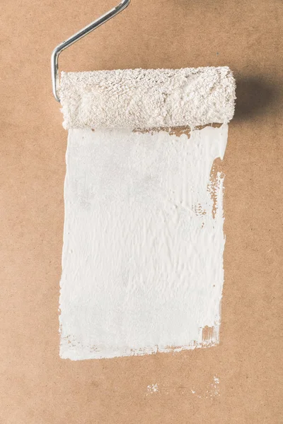 Paint roll brush in white paint on plywood surface — Stock Photo