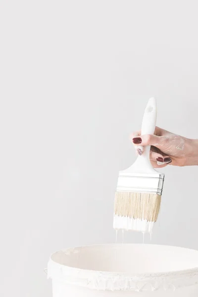 Imagen recortada de la mujer sosteniendo cepillo en pintura blanca por encima de cubo aislado en blanco - foto de stock