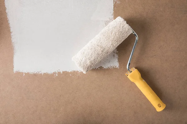 Paint roll brush in white paint on plywood surface — Stock Photo