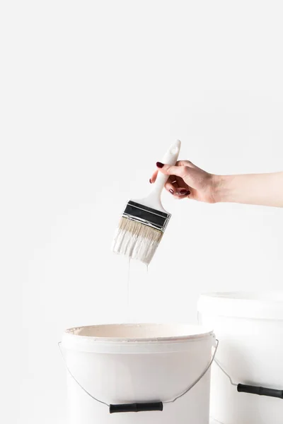 Cropped image of woman holding brush in white paint above buckets isolated on white — Stock Photo