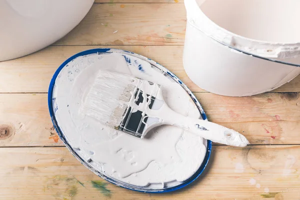 Brush in white paint on cover from bucket — Stock Photo