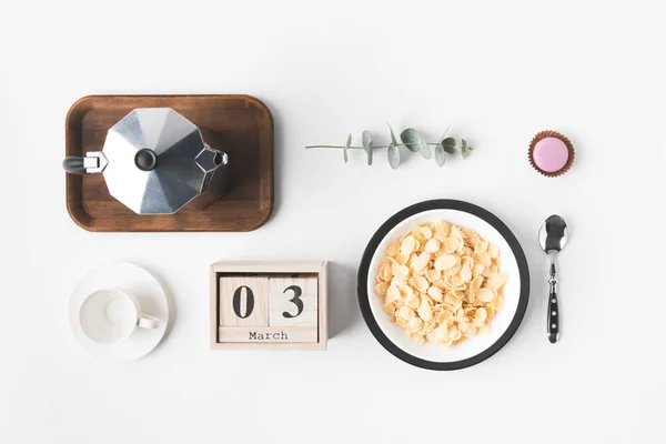 Acostado plano con hojuelas de maíz en un tazón para el desayuno, cafetera y taza de café en la superficie blanca — Stock Photo