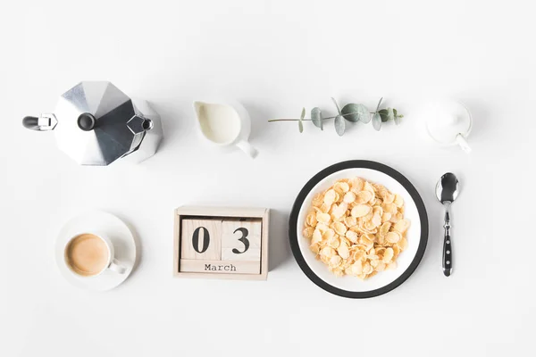 Plano con hojuelas de maíz en tazón para el desayuno, cafetera y calendario en la superficie blanca - foto de stock