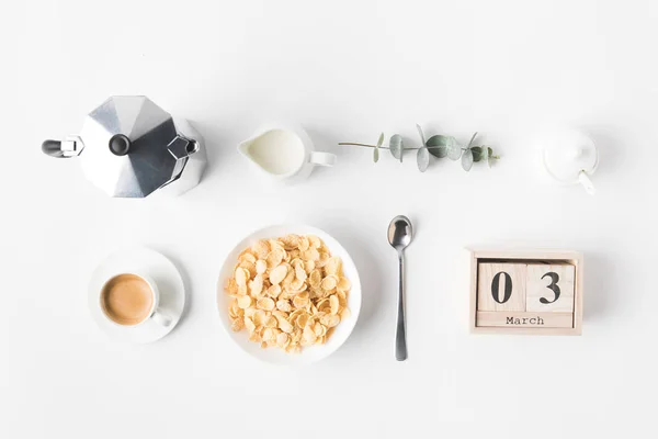 Flat lay com flocos de milho na tigela para o café da manhã, cafeteira e xícara de café na superfície branca — Fotografia de Stock