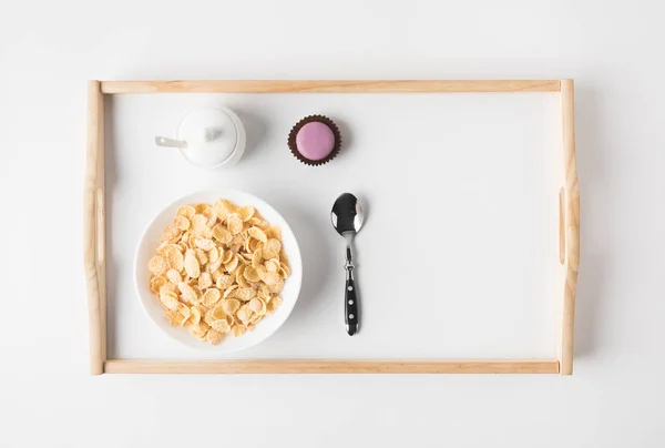 Верхний вид завтрака с пробковыми хлопьями в миске и сладким десертом на подносе на белой поверхности — стоковое фото