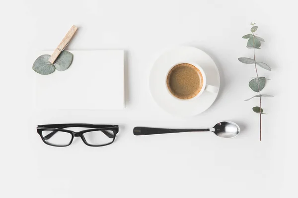 Vista superior de las gafas, taza de café, servilleta y planta en la superficie blanca - foto de stock