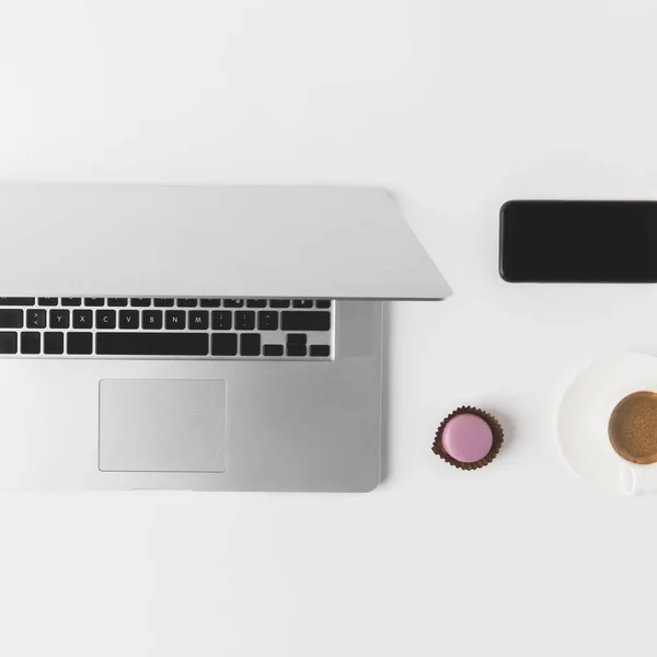 Flache Liege mit Laptop, Smartphone, Tasse Kaffee und Dessert auf weißer Tischplatte — Stockfoto