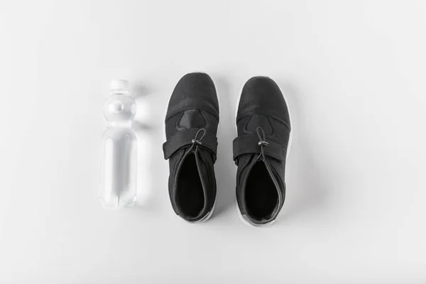 Верхний вид бутылки с водой и кроссовки на белой поверхности — стоковое фото