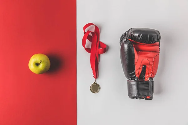 Vue du dessus du gant de boxe avec médaille et pomme sur plateau rouge et blanc — Photo de stock