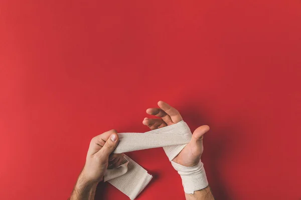 Cropped shot of fighter covering up hands in elastic bandage before fight on red surface — Stock Photo