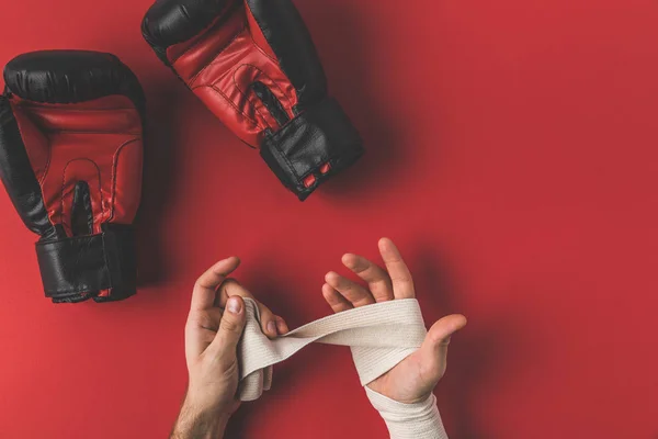 Cropped shot of boxer covering up hands in elastic bandage before fight on red surface — Stock Photo