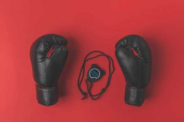 Vue du dessus des gants de boxe avec chronomètre sur plateau rouge — Photo de stock