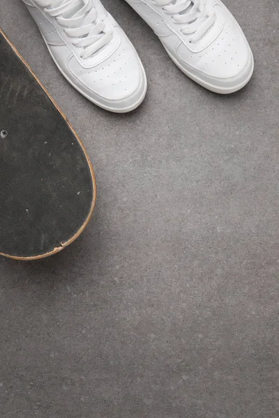Вид сверху на белые кроссовки и скейтборд на серой асфальтовой поверхности — стоковое фото