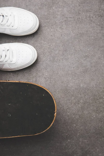 Вид сверху на белые кроссовки и скейтборд на бетонной поверхности — стоковое фото