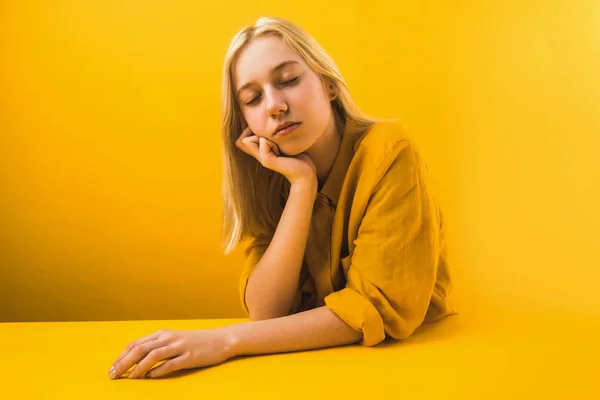 Hermosa mujer joven en ropa amarilla sentado con los ojos cerrados en amarillo - foto de stock